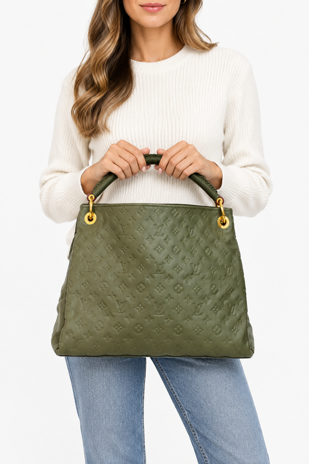 A woman wearing a white ribbed sweater and blue jeans holds a large olive green monogram handbag with gold-tone hardware against a plain light gray background.