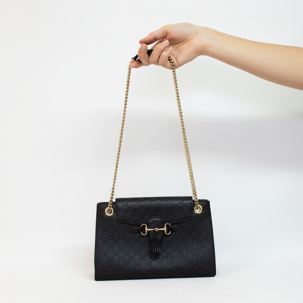 Model hand holding black designer bag by chain